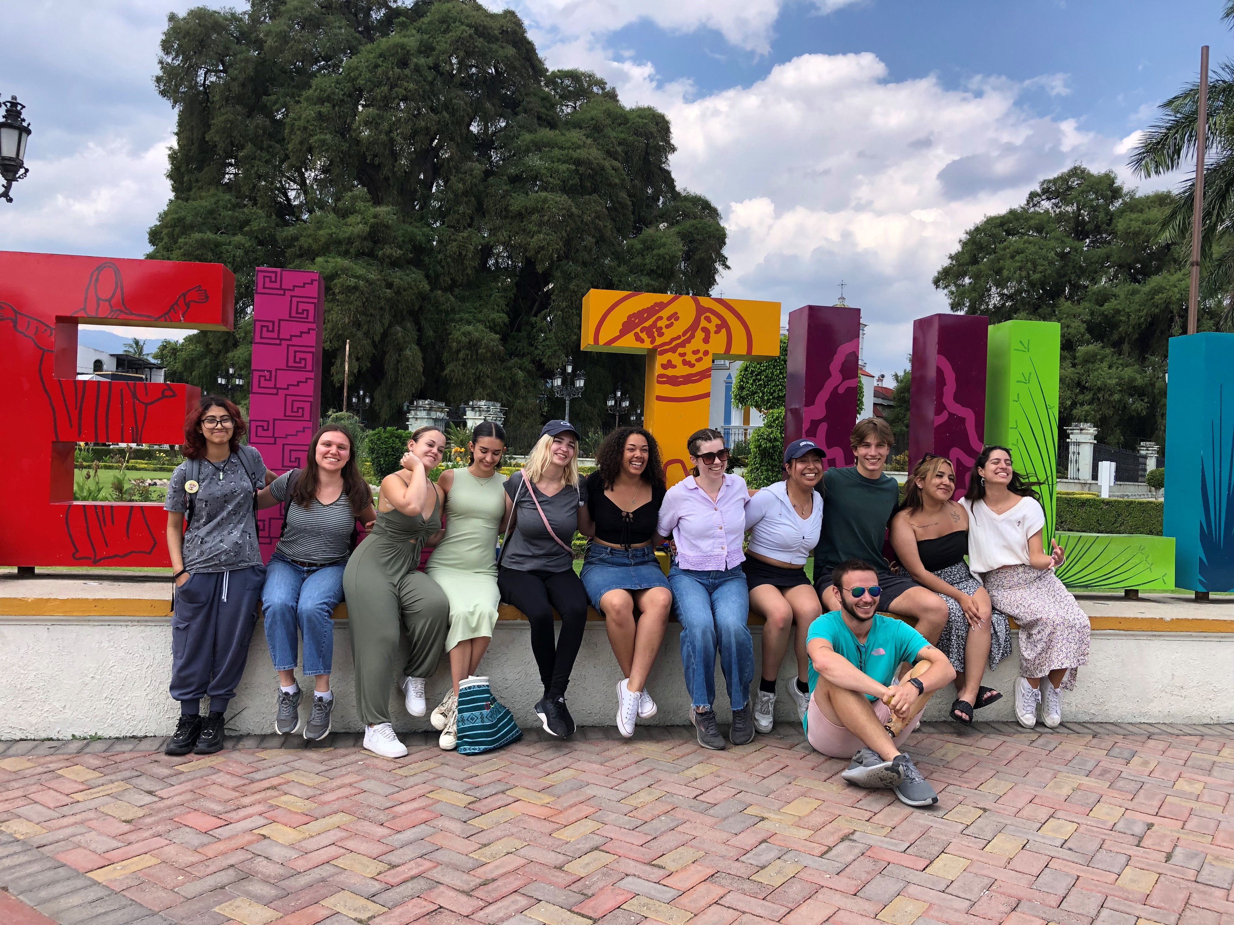 Group photo of twelve students in the Maymester Program on a short wall 